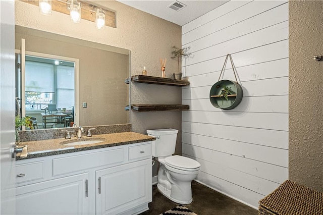 half bath with toilet, a textured wall, vanity, and visible vents