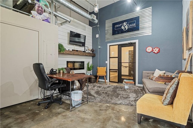 office featuring a towering ceiling, a large fireplace, and unfinished concrete floors