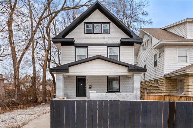 traditional style home featuring covered porch, brick siding, and a fenced front yard