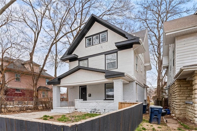 american foursquare style home with covered porch, brick siding, and a fenced front yard