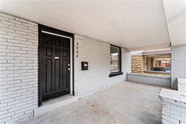 property entrance featuring covered porch and brick siding