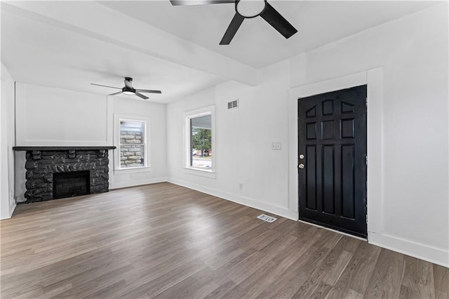 unfurnished living room featuring a stone fireplace, wood finished floors, visible vents, and baseboards