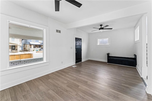 empty room with a ceiling fan, wood finished floors, visible vents, and baseboards