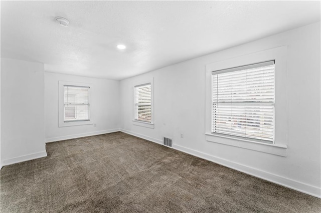 unfurnished room with dark colored carpet, visible vents, a textured ceiling, and baseboards