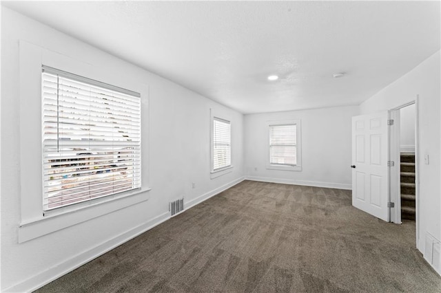 empty room with carpet, visible vents, and baseboards