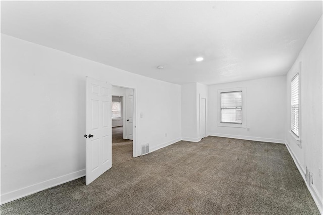 empty room with visible vents, dark carpet, and baseboards