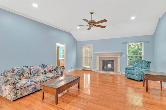 living room with light wood finished floors, lofted ceiling, a tiled fireplace, ceiling fan, and baseboards