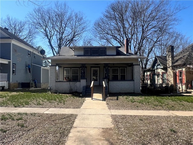 bungalow with a shingled roof, covered porch, and a chimney