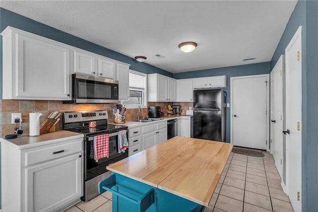 kitchen with light tile patterned flooring, a sink, black appliances, white cabinetry, and tasteful backsplash