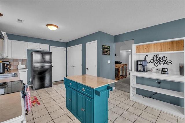 kitchen featuring electric range, light tile patterned flooring, blue cabinetry, freestanding refrigerator, and light countertops