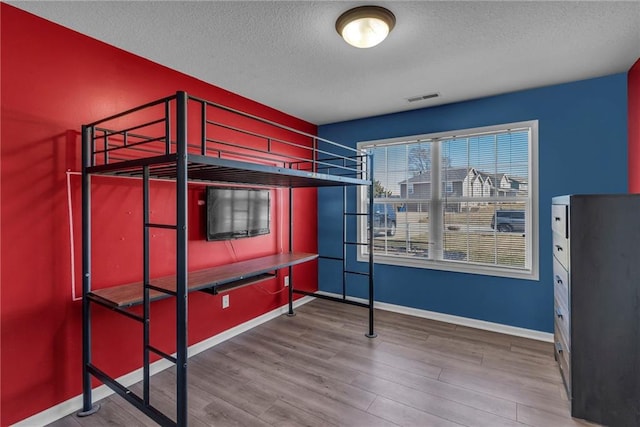 bedroom with visible vents, baseboards, a textured ceiling, and wood finished floors