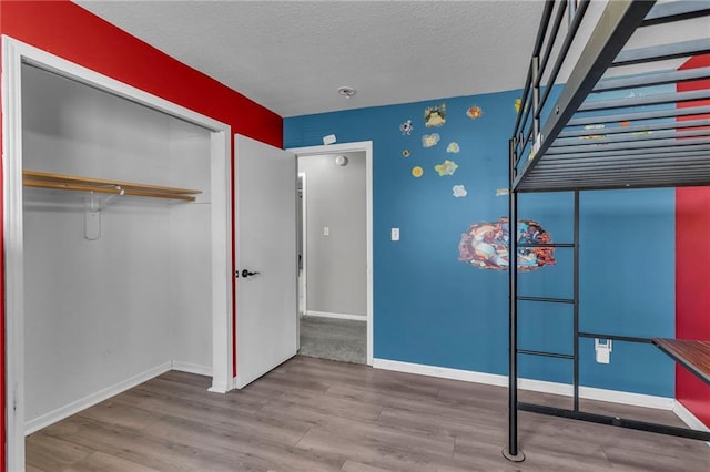 unfurnished bedroom featuring a closet, baseboards, a textured ceiling, and wood finished floors