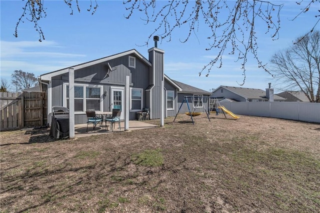 rear view of property featuring a lawn, a patio, a fenced backyard, a playground, and a chimney