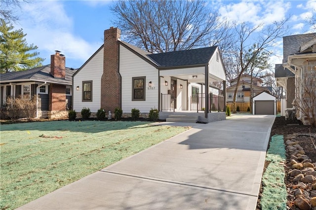 view of front facade featuring driveway, an outdoor structure, a front yard, a garage, and a chimney