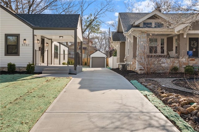 view of property exterior featuring covered porch, driveway, an outdoor structure, and roof with shingles