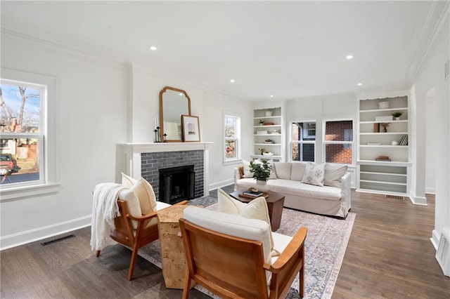 living area featuring visible vents, ornamental molding, built in features, baseboards, and a brick fireplace