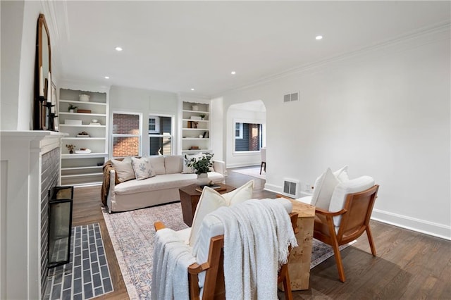 living area featuring ornamental molding, a fireplace, visible vents, and arched walkways