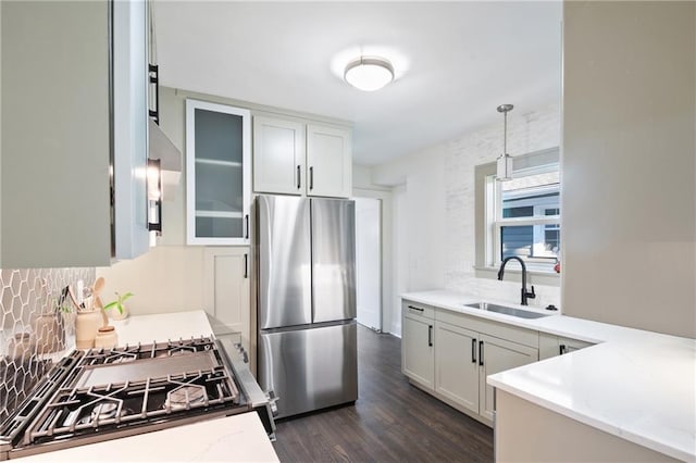 kitchen with light stone countertops, decorative backsplash, appliances with stainless steel finishes, dark wood-style floors, and a sink