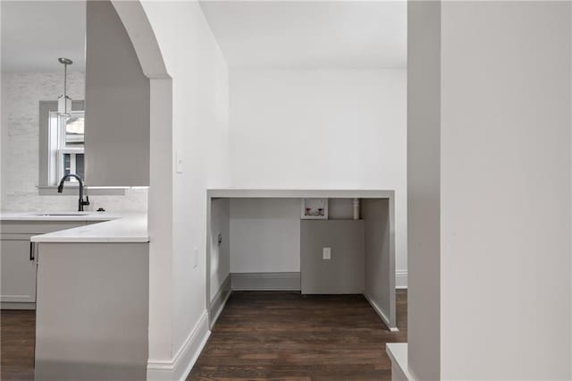 interior space with a sink, arched walkways, laundry area, baseboards, and dark wood-style flooring