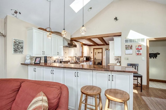 kitchen featuring a peninsula, a skylight, wall chimney exhaust hood, and a kitchen breakfast bar