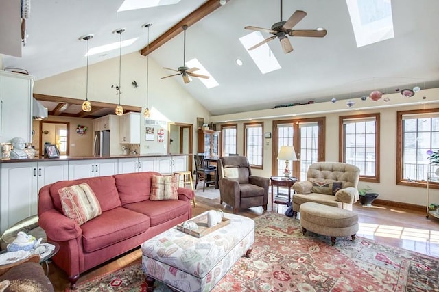 living room featuring a ceiling fan, beam ceiling, a skylight, and light wood-style flooring