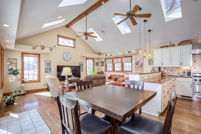 dining space featuring a ceiling fan, high vaulted ceiling, dark wood finished floors, beam ceiling, and a skylight