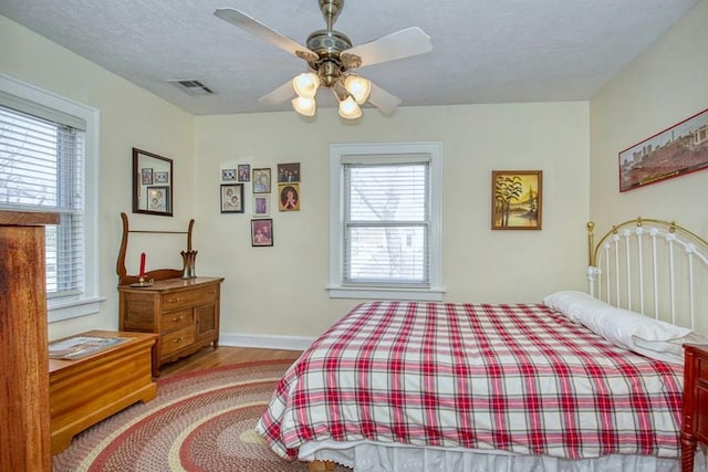 bedroom with visible vents, multiple windows, a textured ceiling, and wood finished floors