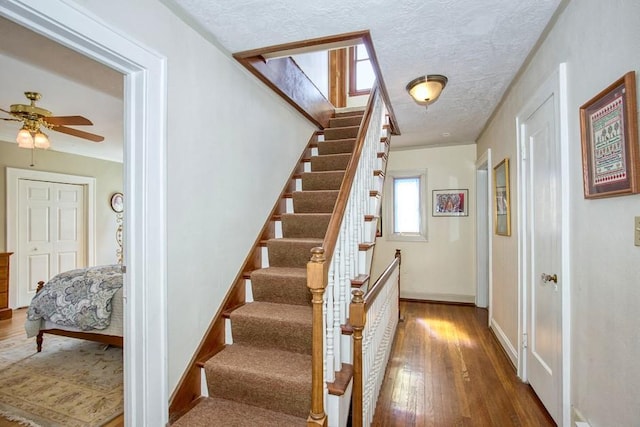 stairway with baseboards, a textured ceiling, a ceiling fan, and wood finished floors