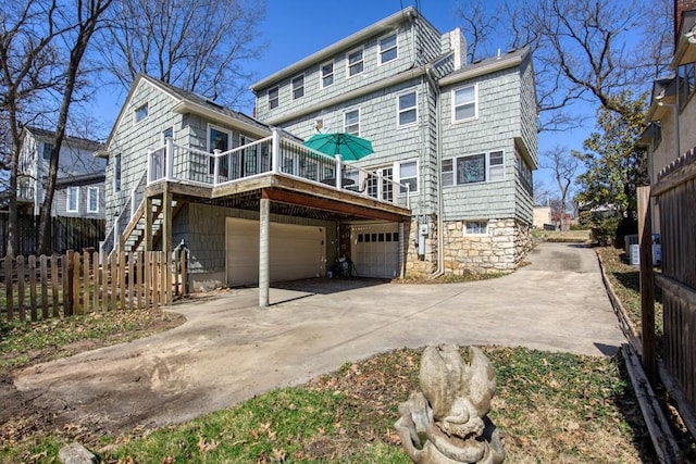 rear view of house with fence, concrete driveway, an attached garage, a wooden deck, and stairs