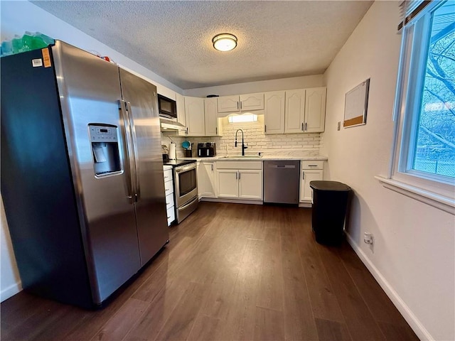 kitchen featuring dark wood finished floors, a sink, appliances with stainless steel finishes, white cabinetry, and tasteful backsplash