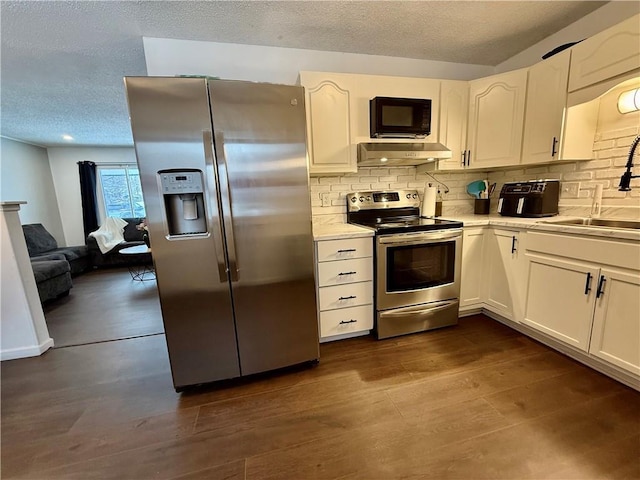 kitchen with a sink, under cabinet range hood, light countertops, stainless steel appliances, and dark wood-style flooring