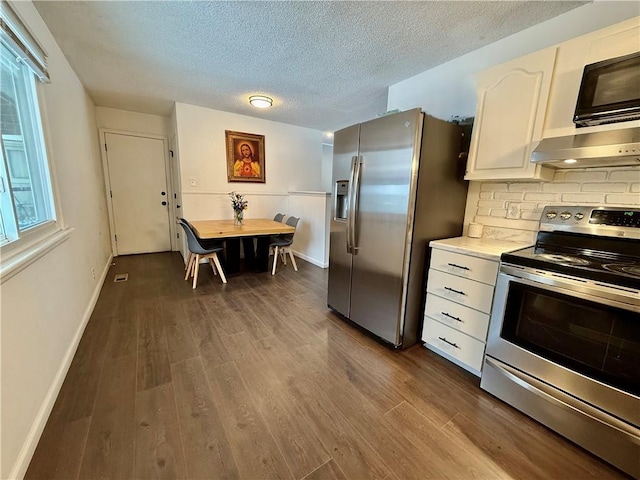 kitchen with dark wood-type flooring, light countertops, range hood, appliances with stainless steel finishes, and white cabinets