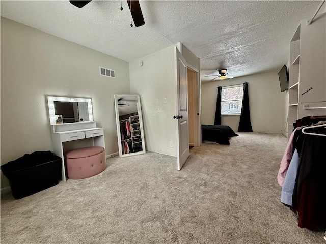 carpeted bedroom with visible vents, a textured ceiling, and ceiling fan