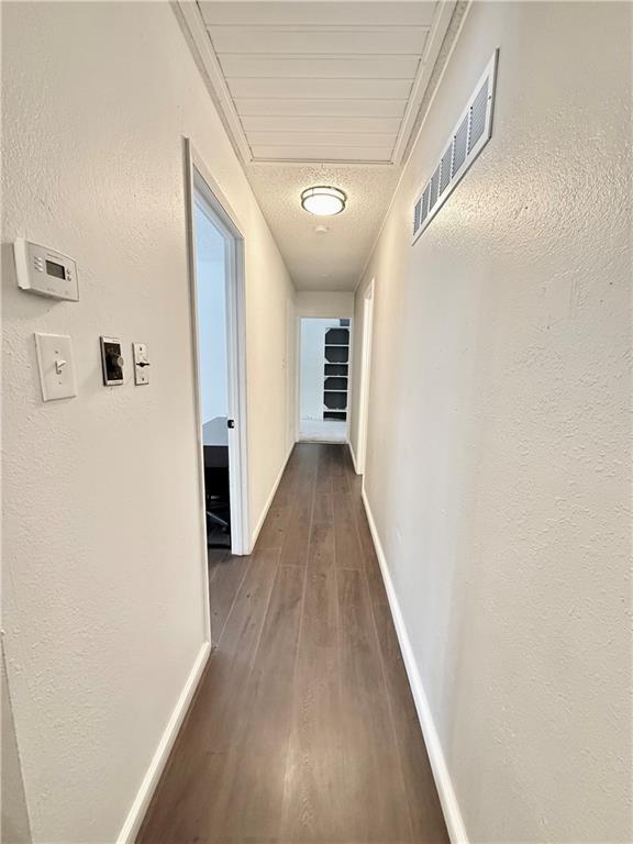 hall featuring baseboards, visible vents, dark wood finished floors, a textured ceiling, and a textured wall