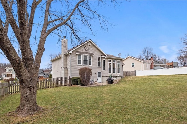 back of property with a chimney, a fenced backyard, and a lawn