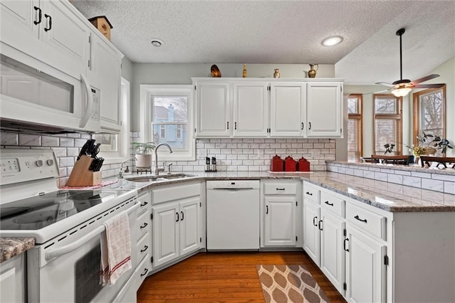 kitchen featuring white cabinets, a sink, wood finished floors, white appliances, and a peninsula