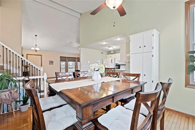 dining space with light wood finished floors, stairway, a ceiling fan, high vaulted ceiling, and baseboards