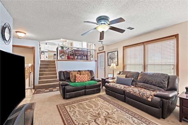 living room featuring ceiling fan, a textured ceiling, light colored carpet, visible vents, and stairway