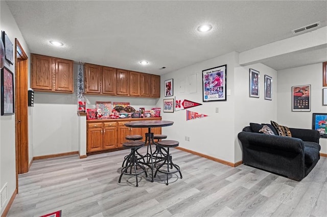 interior space featuring baseboards, visible vents, brown cabinetry, a textured ceiling, and light wood-style floors