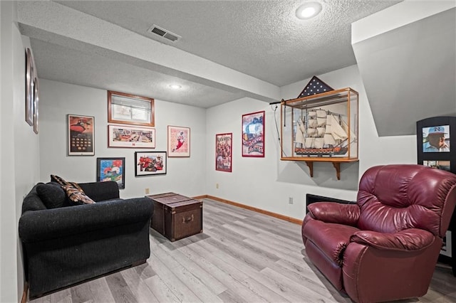 living room featuring baseboards, a textured ceiling, visible vents, and wood finished floors