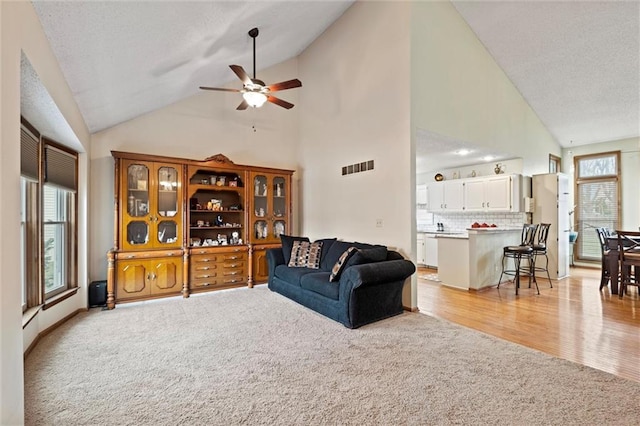 living area featuring a ceiling fan, visible vents, light carpet, and a textured ceiling