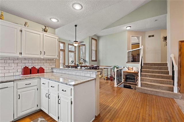 kitchen with vaulted ceiling, a peninsula, white dishwasher, and white cabinets