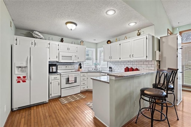 kitchen featuring a peninsula, white appliances, a healthy amount of sunlight, and white cabinets