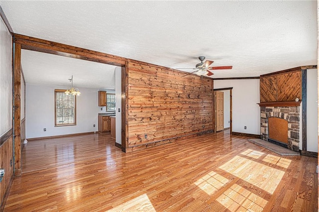 unfurnished living room with ceiling fan with notable chandelier, light wood-style flooring, a fireplace, and a textured ceiling