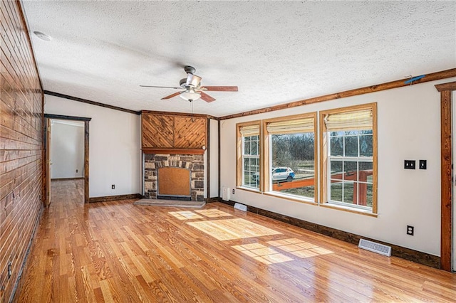 unfurnished living room featuring a stone fireplace, light wood-style flooring, a textured ceiling, and visible vents