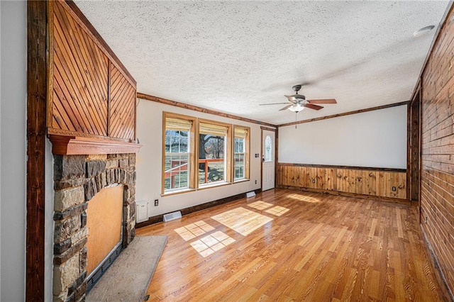 interior space with crown molding, a wainscoted wall, a stone fireplace, light wood-style flooring, and a textured ceiling