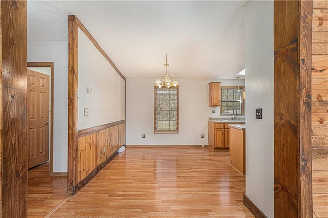 unfurnished dining area featuring wooden walls, wainscoting, light wood-style flooring, a notable chandelier, and a textured ceiling