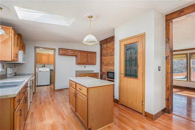 kitchen with white appliances, light wood finished floors, a skylight, washer / clothes dryer, and light countertops