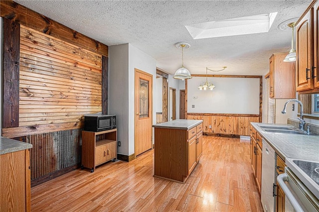 kitchen with a wainscoted wall, light wood finished floors, a skylight, a sink, and wood walls