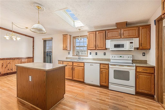 kitchen featuring white appliances, vaulted ceiling with skylight, light wood finished floors, and a sink